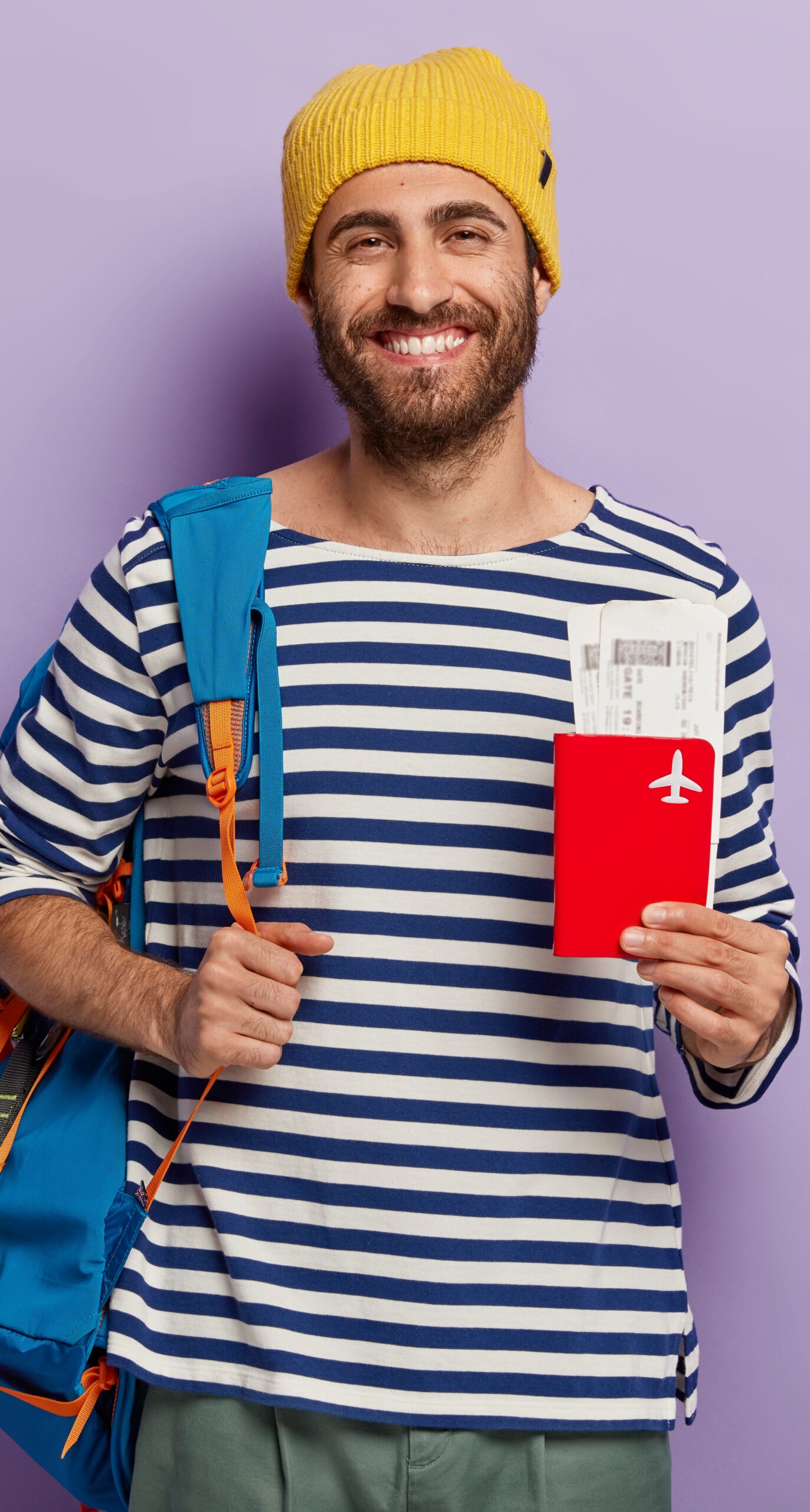 Indoor shot of optimistic tourist holds passport and tickets, carries rucksack, waits for flight, ready for vacation, enjoys travel, receives visa for traveling abroad, dressed in casual outfit